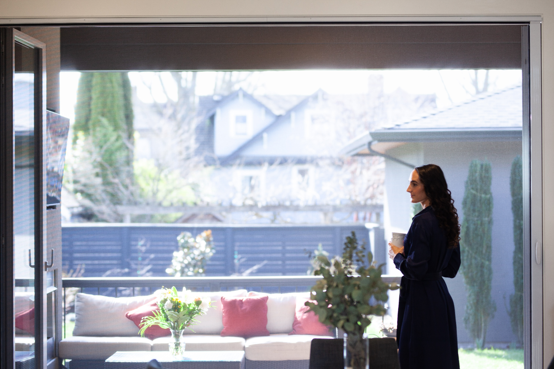 Woman enjoying bug-free patio with Mirage 3500 screen doors and outdoor furniture